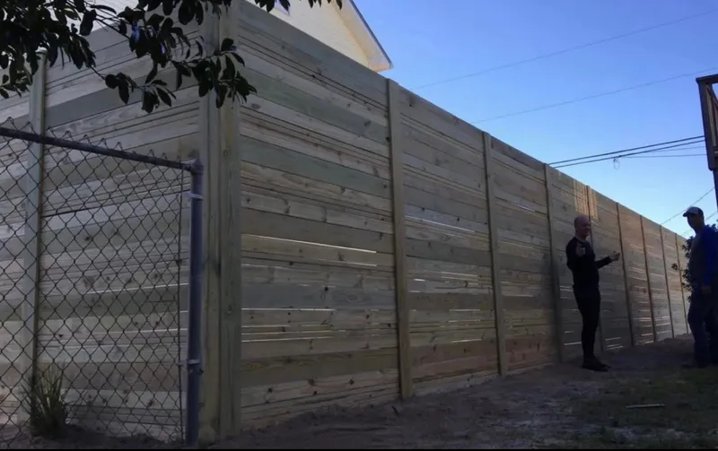 A custom 8 foot tall pine privacy fence with horizontal boards running the length of a backyard, two men standing at its base for scale, built by Southern Line Fence & Finish