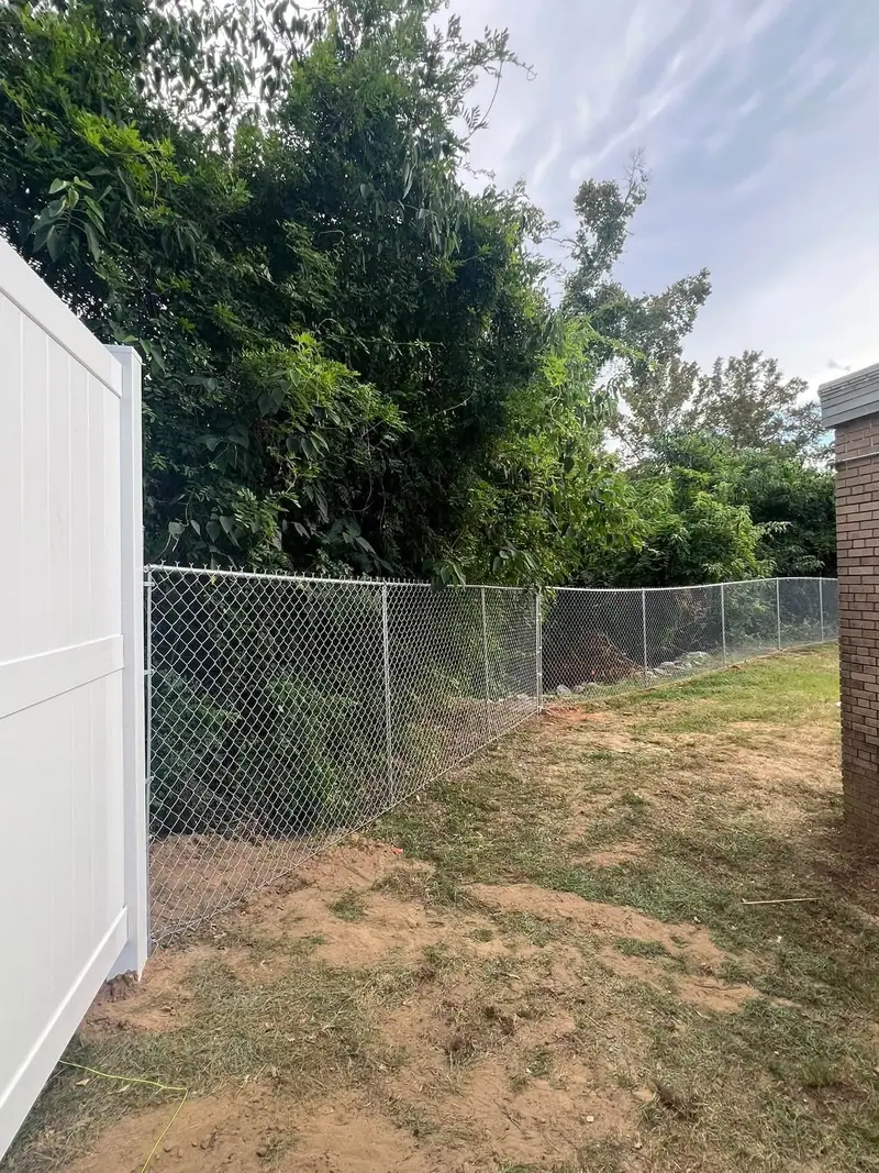 New white vinyl privacy fence meeting an existing chain link fence at the back of a yard