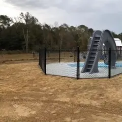 Black chain link pool fence around a new pool with a slide, house behind