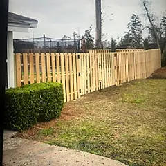 Shadowbox pine fence behind a trimmed hedge beside a house